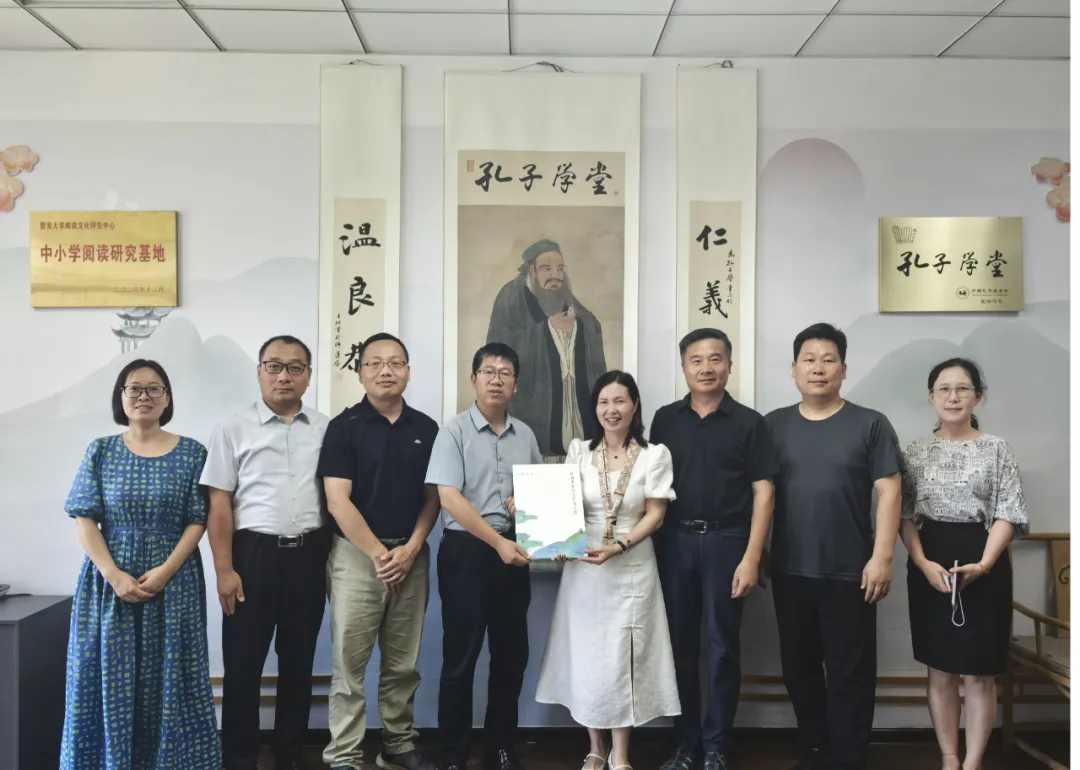 Eight people pose for a group photo against a Confucius Classroom backdrop; two central figures hold documents